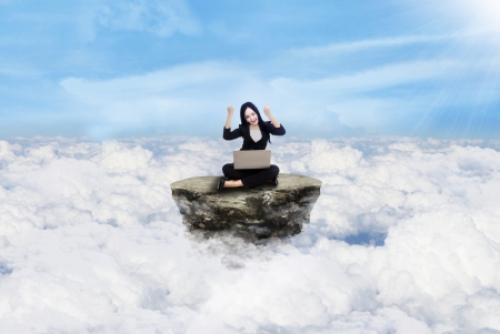 Happy beautiful businesswoman sitting on the rock above cloudsの写真素材