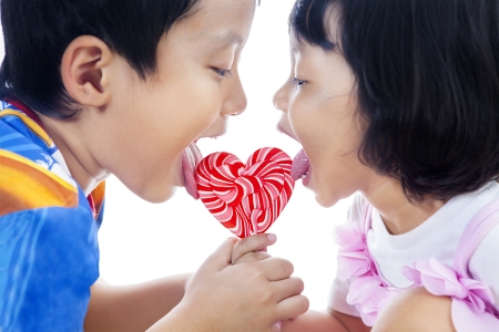 Brother and sister are licking heart shape lollipop on white backgroundの写真素材