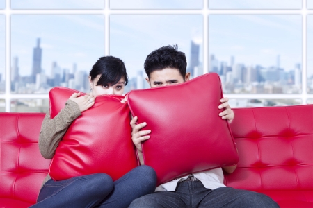Couple hide behind pillow on red sofaの写真素材