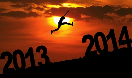 Silhouette of a man jumping from 2013 towards 2014 year at sunsetの写真素材