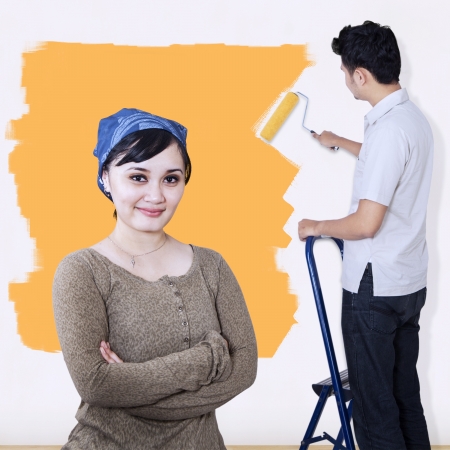 Girlfriend looking at camera while boyfriend painting wall in yellowの写真素材