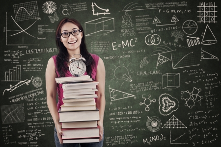 Asian student is holding stack of books and clock in the classroomの写真素材