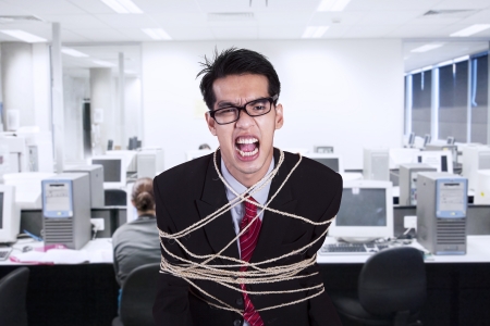 Angry businessman tied with rope at the officeの写真素材