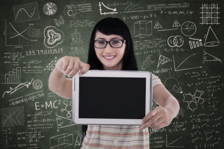 Beautiful female student is showing blank screen of e-tablet in classの写真素材