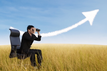 Businessman using binoculars looking for growing chart cloud on fieldの写真素材