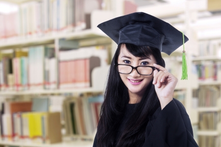 Asian graduate in graduation gown with glasses pose at libraryの写真素材