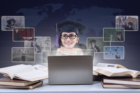 Happy female graduate with laptop and online pictures on world map backgroundの写真素材