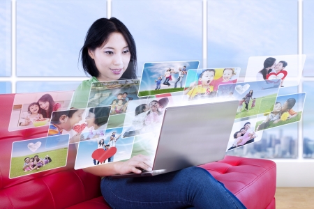 Beautiful female is looking at online photos in laptop inside an apartmentの写真素材
