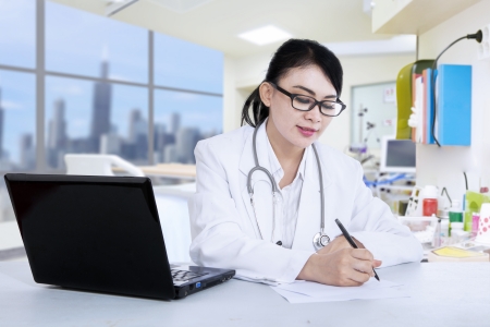 Attractive female doctor is writing prescription at the clinicの写真素材