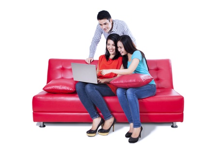 A group of college friends with laptop and sitting on red sofaの写真素材