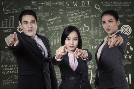 Excited young business people pointing at you on chalkboardの写真素材
