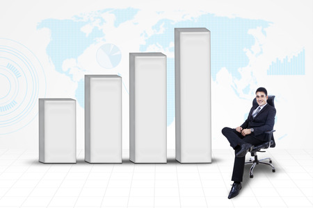 Asian businessman sitting on chair with bar chart on world map backgroundの写真素材