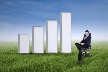 Smiling asian businessman with business growth chart on the meadowの写真素材