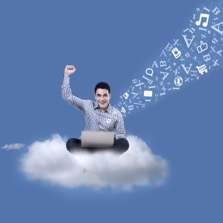 Asian male student sitting on a cloud under blue sky with laptop and flying lettersの写真素材