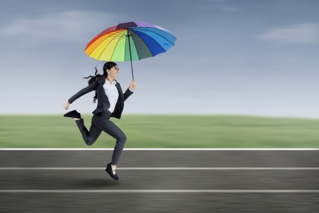 Beautiful businesswoman running under an umbrella on the running trackの写真素材