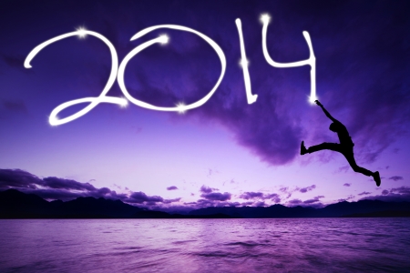 Young man jumping and drawing 2014 on the beachの写真素材