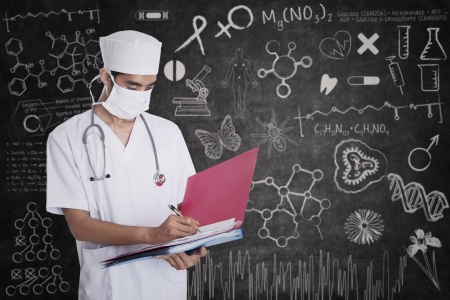 Male doctor standing with a folder on blackboard backgroundの写真素材