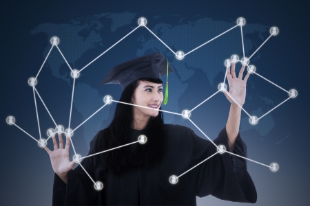 Beautiful female graduate with social network touchscreen concept on blue world map backgroundの写真素材