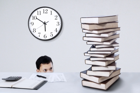 Young businessman looking at stack of books on the deskの写真素材