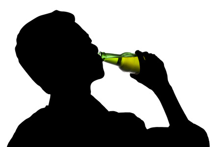 Silhouette of drunk man drinking a bottle of beerの写真素材