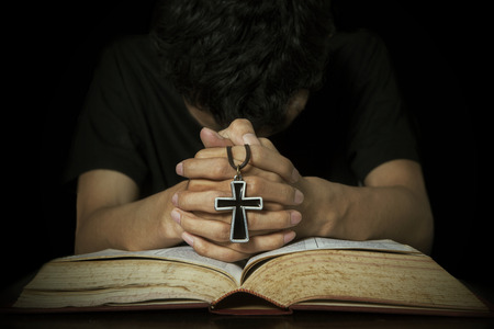 Closeup of man praying on bible while holding a crossの写真素材
