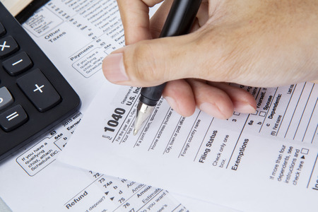 Person completing 1040 tax form with calculator and penの写真素材