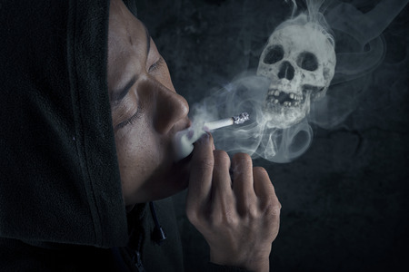 Young man smoking cigarette on dark backgroundの写真素材