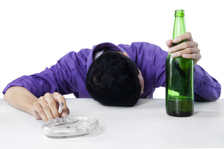 Drunk man sleeping on the table while holding cigarette, with a glass and bottle of beer