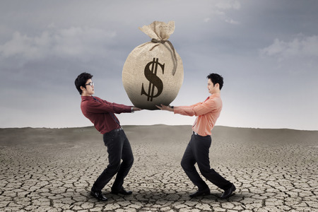 Two business people carrying a money bag with US dollar signの写真素材