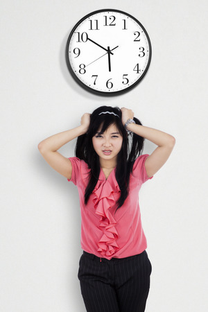 Portrait of stressed employee grabbing her hair under a clock on the wallの写真素材