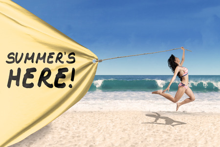 Happy woman jumping on the beach while pulling a banner of summertimeの写真素材