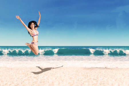 Happy woman wearing bikini jumping on the beach. Shoot at summertimeの写真素材