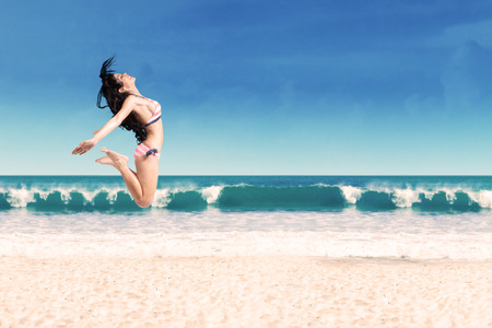 Excited woman leaping at beach. Shoot at summertimeの写真素材