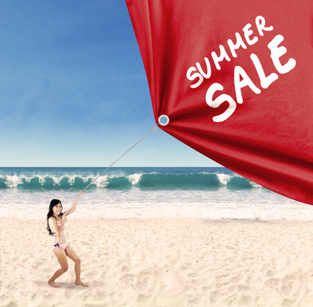 Happy woman jumping on the beach while pulling a banner of summer saleの写真素材