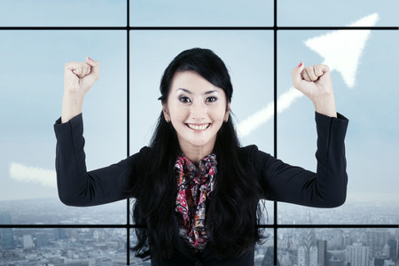 Businesswoman celebrating success in front of a window with an upward arrowの写真素材