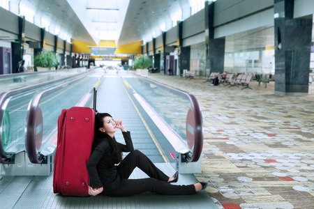 Businesswoman sitting on the floor with a suitcase in airportの写真素材