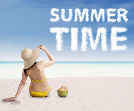 Sexy young woman in straw hat looking at a text of summer time on the beachの写真素材