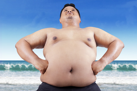 Fat man with big stomach standing on beachの写真素材