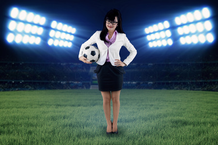 Full length female football manager holding a soccer ball at fieldの写真素材