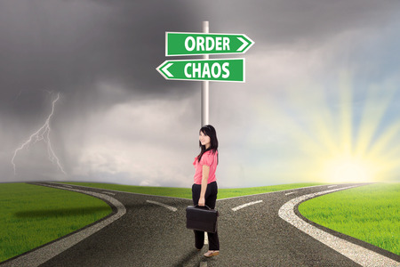 Businesswoman standing on the road with signpost of order and chaosの写真素材