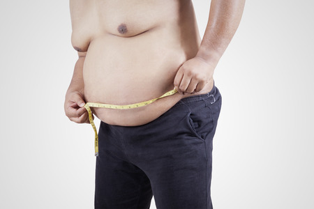 Obese person measuring his belly, isolated on white backgroundの写真素材