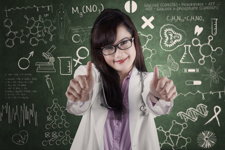 Attractive doctor showing thumbs-up in front of medical backgroundの写真素材