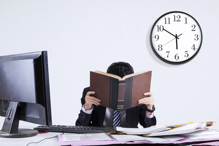Portrait of exhausted businessman because overworked covering his face by a bookの写真素材