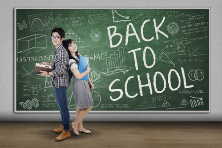 Group of student standing in the class with a text of back to school on blackboardの写真素材