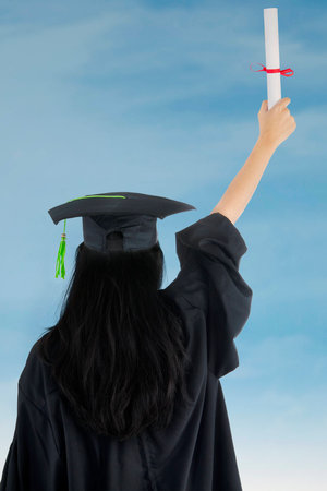 Woman in graduation gown rejoicing success. rear viewの写真素材