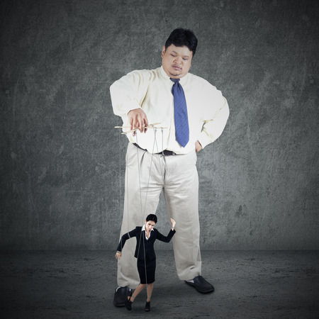 Businesswoman hanging on string and controlled by a businessmanの写真素材