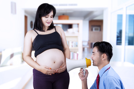 Asian father uses a megaphone for calling his baby on his wife's tummy, shot at home