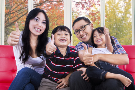 Attractive hispanic family smiling and showing tumbs-up at camera with autumn background on the windowの写真素材