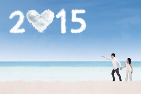 Two people holding hands on the beach and pointing at cloud shaped number 2015の写真素材