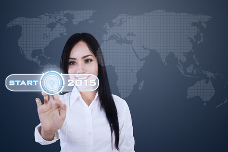 Beautiful businesswoman pushing a start button of future 2015 on a virtual screenの写真素材